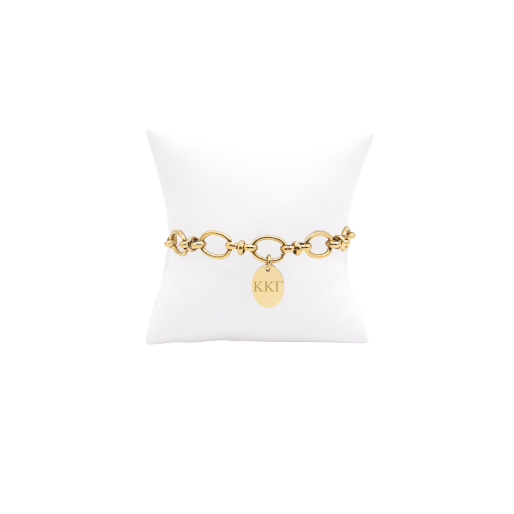 Kappa Kappa Gamma gold large link evermore bracelet with small oval charm with horizontal greek letters on white pillow front view.
