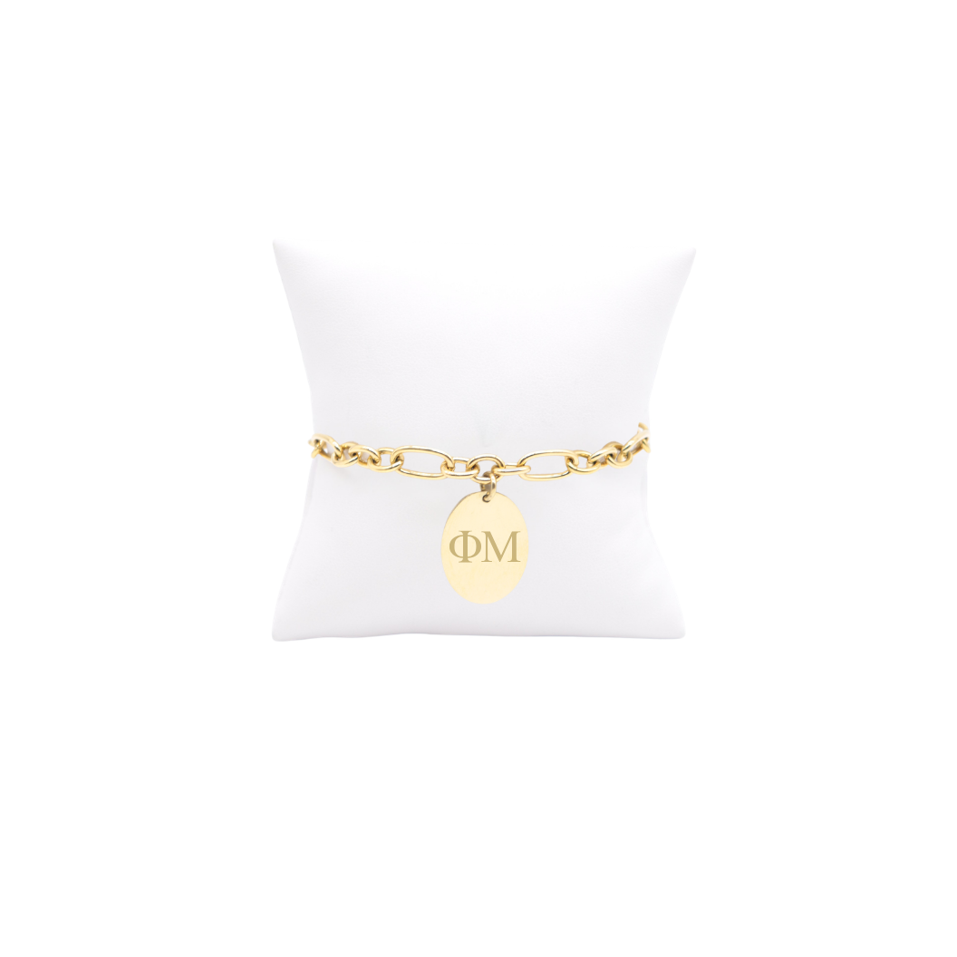 Phi Mu gold large link Keepsake bracelet with large oval charm with horizontal greek letters on white pillow front view
