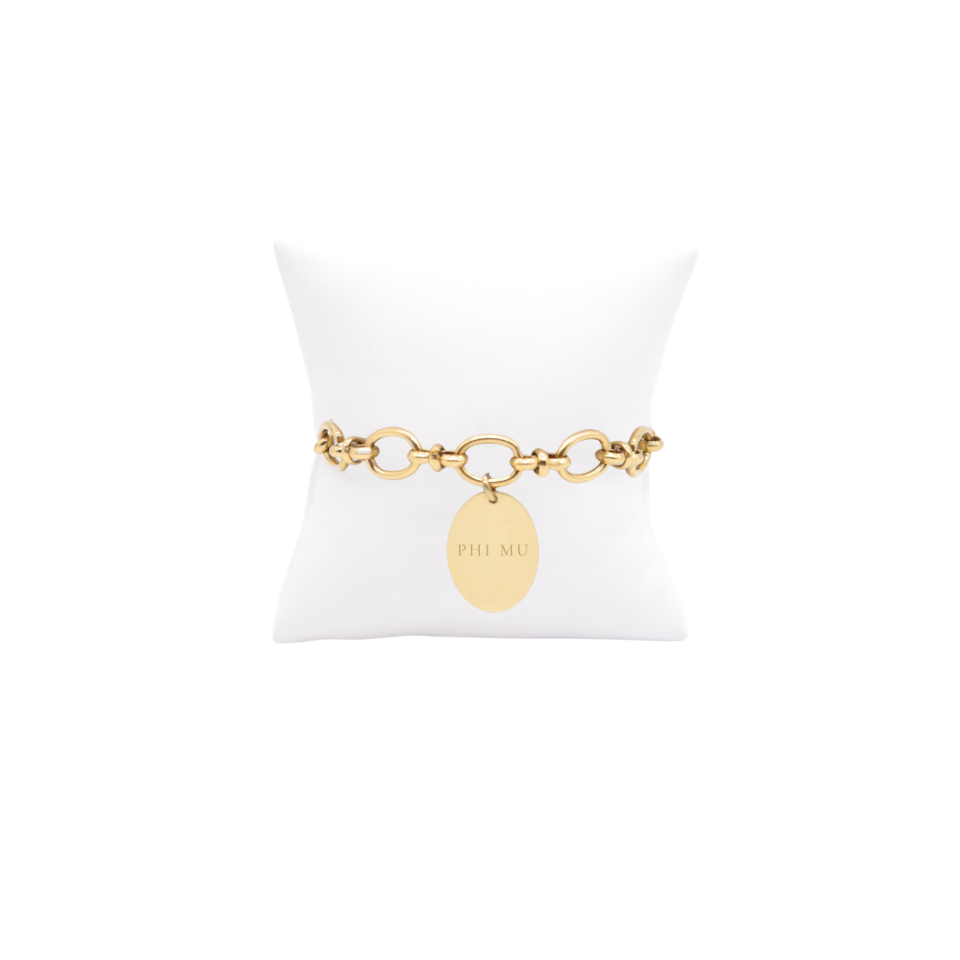 Phi Mu gold large link evermore bracelet with large oval charm with full sorority name on white pillow front view