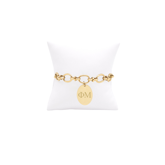 Phi Mu gold large link evermore bracelet with large oval charm with horizontal greek letters on white pillow front view
