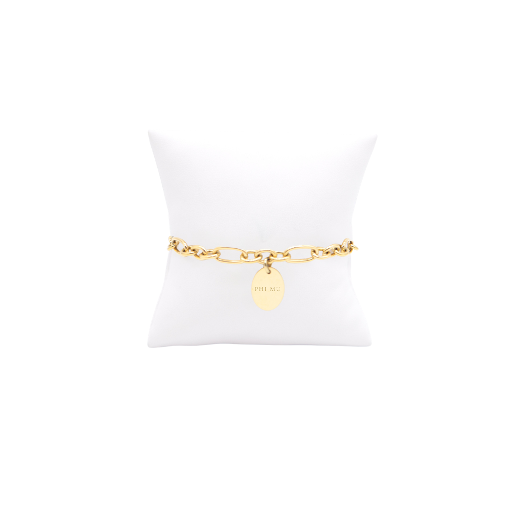 Phi Mu gold link Keepsake bracelet with small oval charm with full sorority name on white pillow front view
