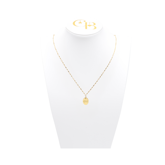 Phi Mu gold twist necklace with small oval charm with horizontal greek letters on white pillow front view
