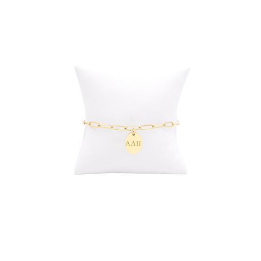 Alpha Delta Pi gold link storyline bracelet with small oval charm with horizontal greek letters on white pillow front view.