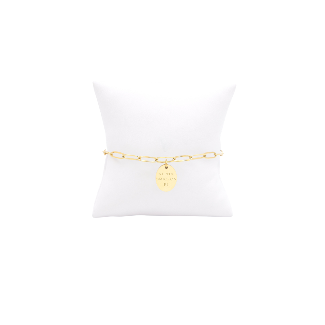 Alpha Omicron Pi gold link storyline bracelet with small oval charm with full sorority name on white pillow front view