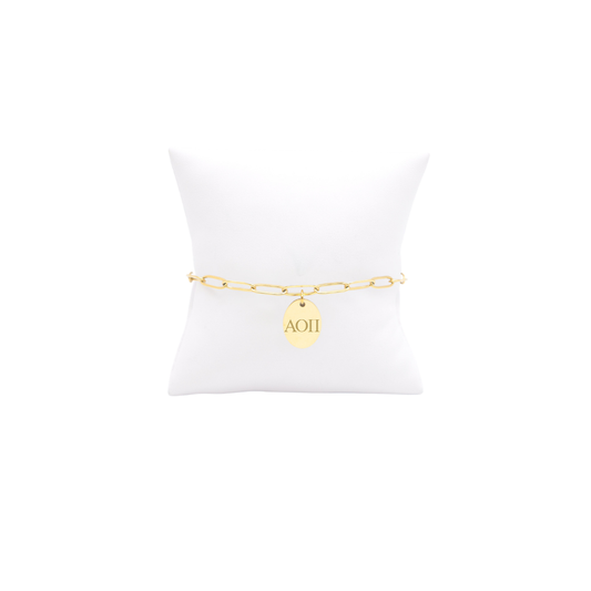 Alpha Omicron Pi gold link storyline bracelet with small oval charm with horizontal greek letters on white pillow front view