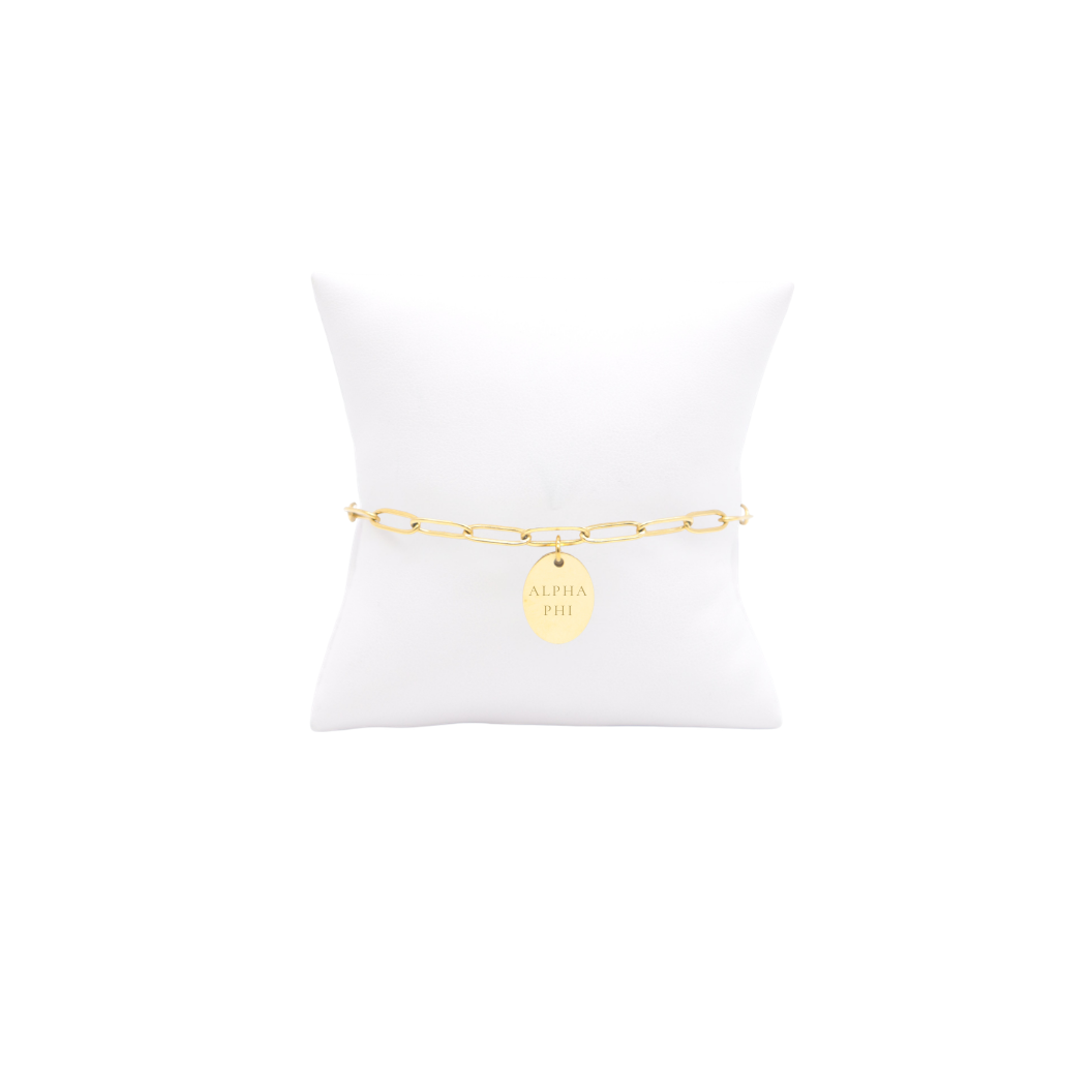 Alpha Phi gold link storyline bracelet with small oval charm with full sorority name on white pillow front view
