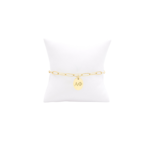 Alpha Phi gold link storyline bracelet with small oval charm with horizontal greek letters on white pillow front view