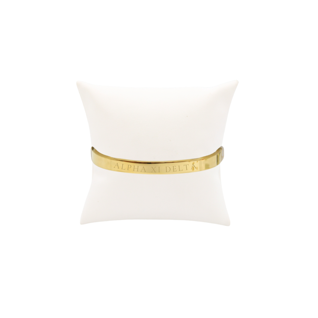 Alpha XI Delta gold bangle bracelet displayed on white pillow front view with full sorority name