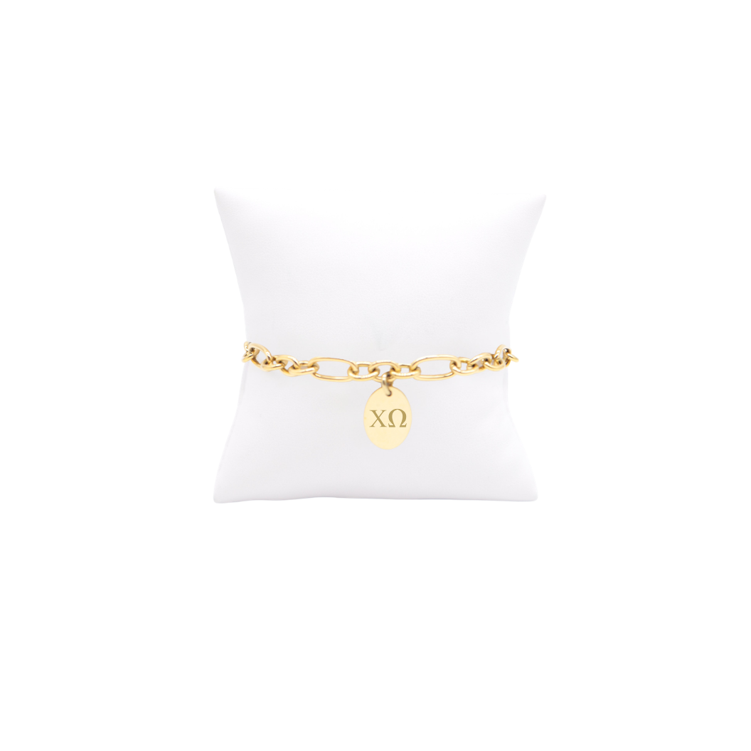 Chi Omega gold link Keepsake bracelet with small oval charm with horizontal greek letters on white pillow front view
