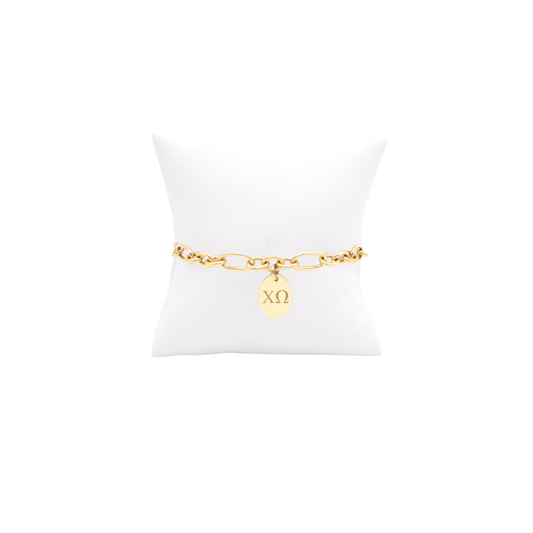Chi Omega gold link Keepsake bracelet with small oval charm with horizontal greek letters on white pillow front view

