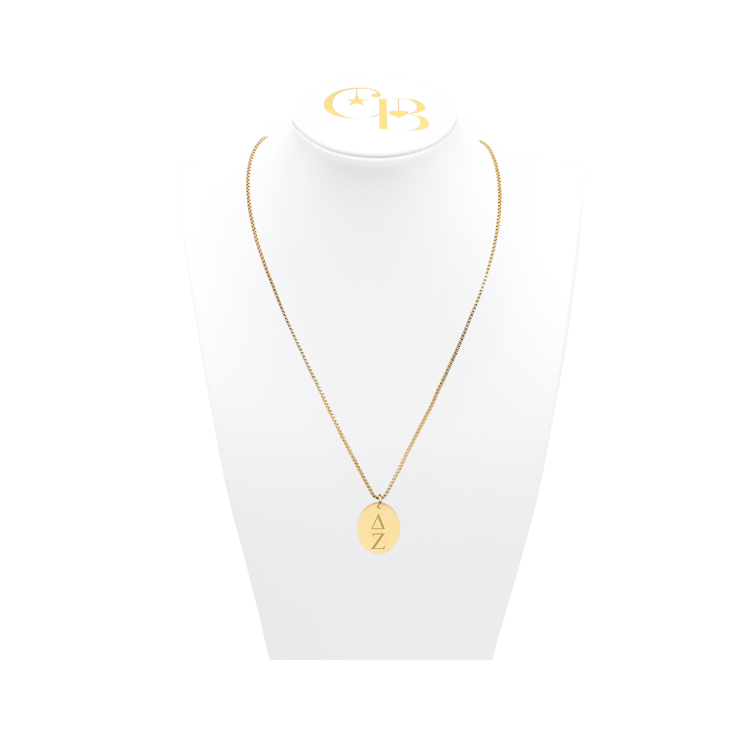 Delta Zeta gold box chain necklace with large oval charm displayed on which necklace bust front view with vertical greek letters