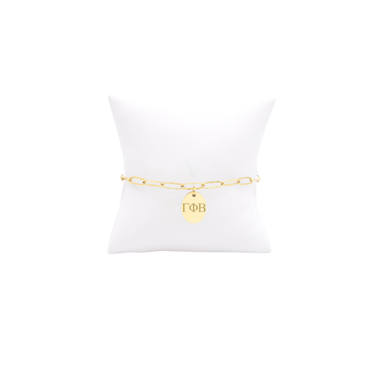 Gamma Phi Beta gold link storyline bracelet with small oval charm displayed on white pillow front view with horizontal greek letters