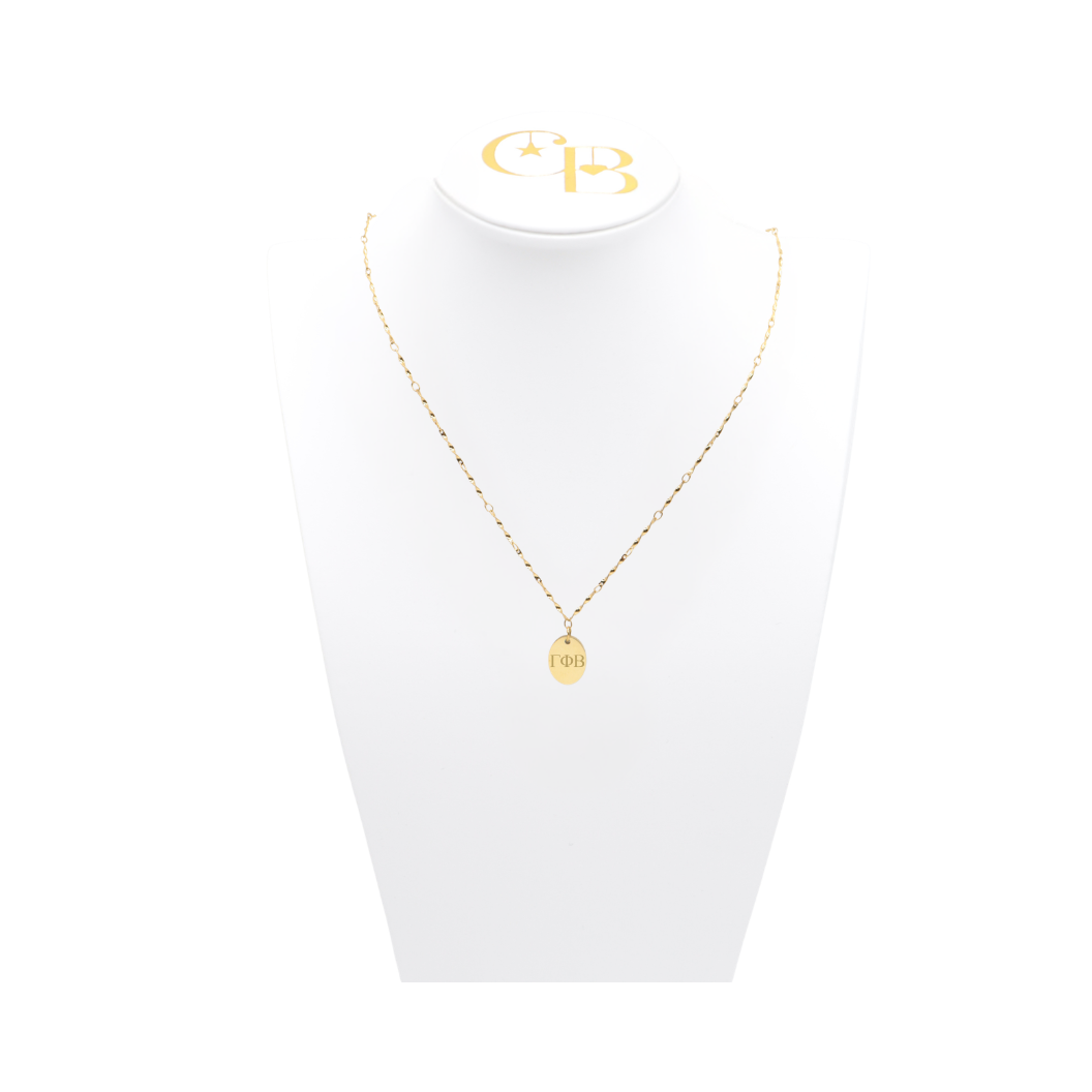Gamma Phi Beta gold simple twist necklace with small oval charm displayed on white pillow front view with horizontal greek letters
