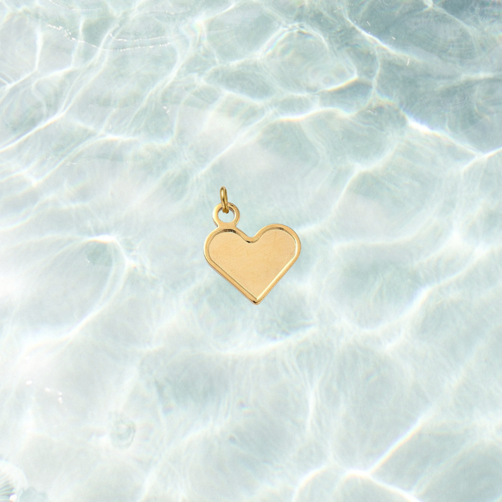 Gold classic heart-shaped charm with a smooth polished finish on a shimmering water background.