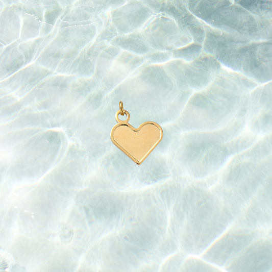 Gold classic heart-shaped charm with a smooth polished finish on a shimmering water background.