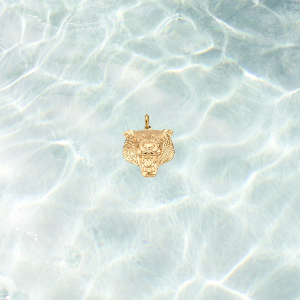 Gold fierce tiger head charm with detailed engraved features on a shimmering water background.