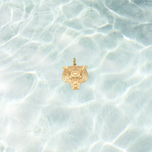 Gold fierce tiger head charm with detailed engraved features on a shimmering water background.