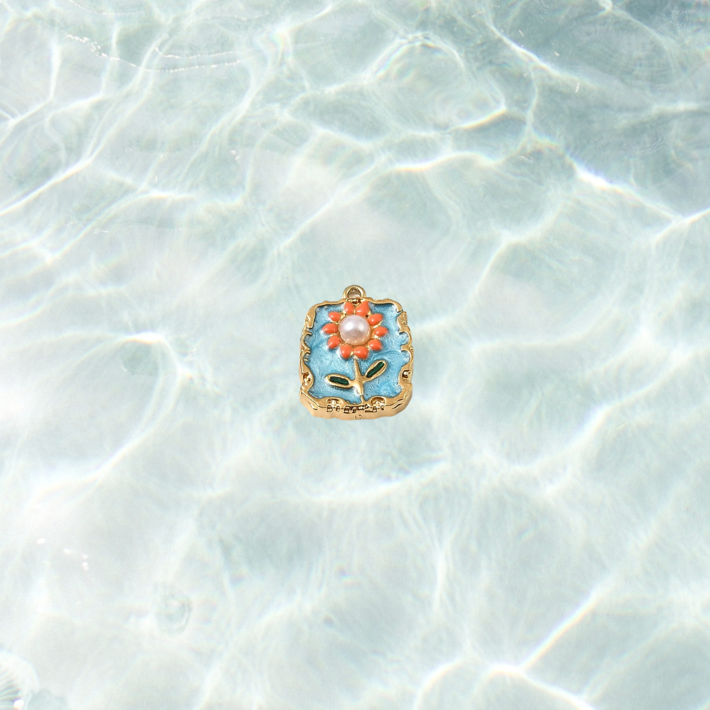 Gold square floral tile charm with pearl tile charm with blue enamel background, orange flower details and pearl center on a waterproof background