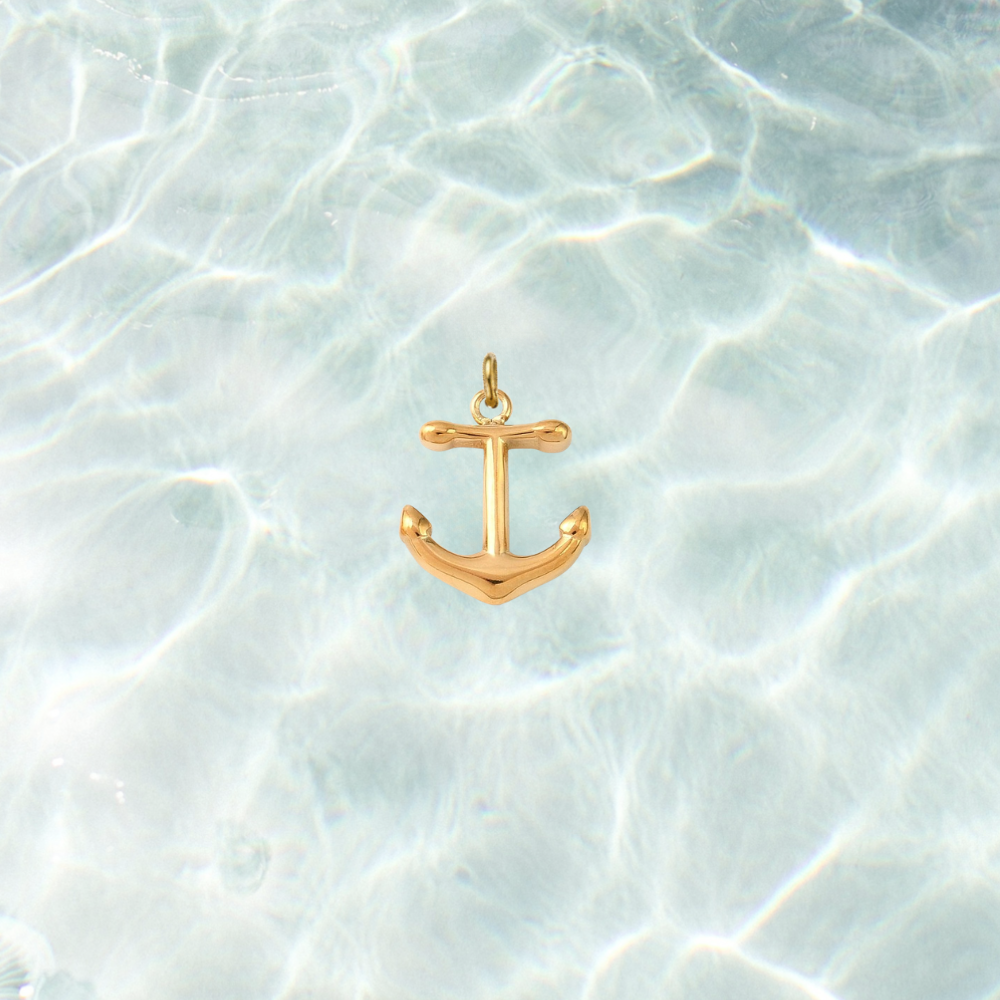 Gold nautical anchor charm with a polished finish on a shimmering water background.