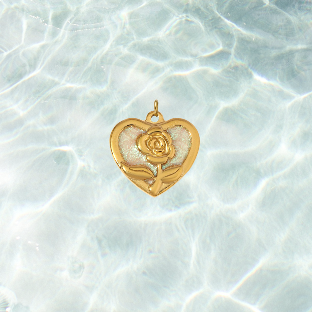 Gold heart-shaped charm featuring a raised rose design over a shimmering iridescent enamel background, displayed on a shimmering water background.