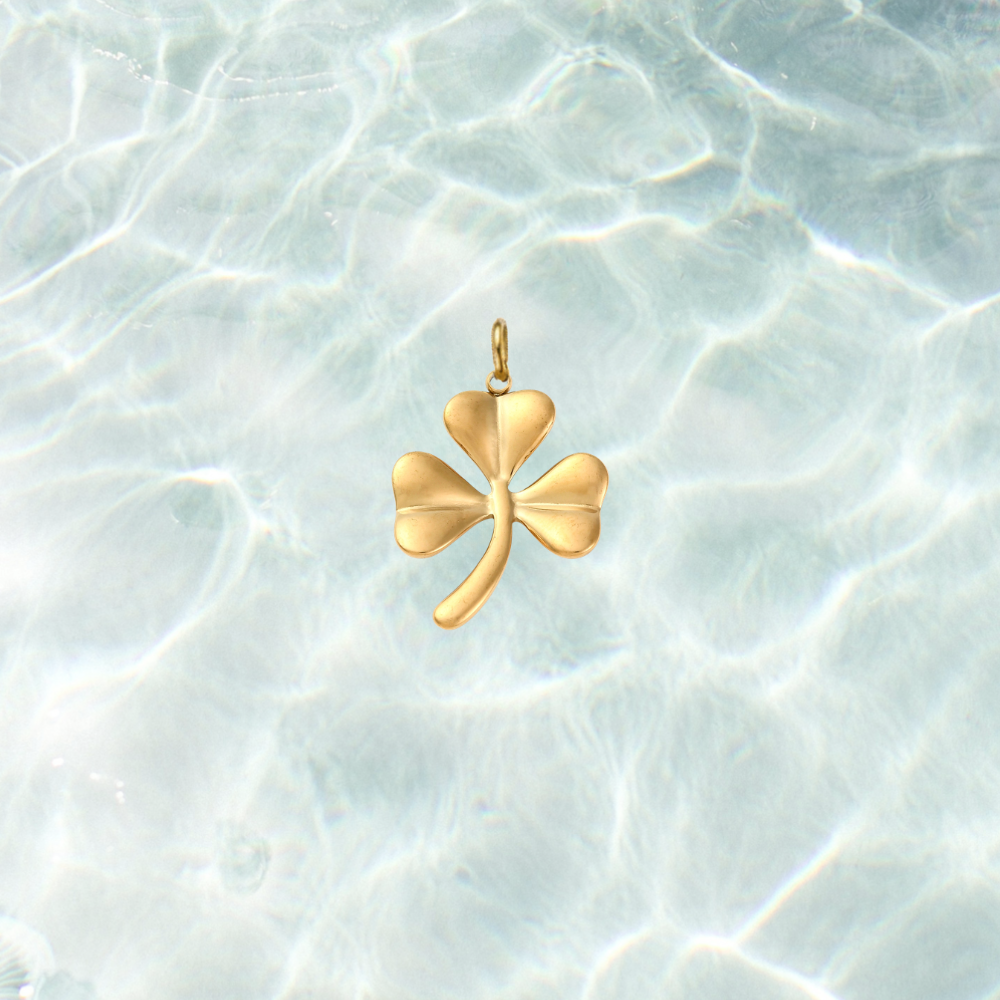 Gold shamrock charm featuring a polished three-leaf clover design on a shimmering water background.