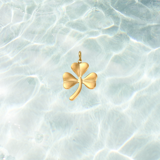 Gold shamrock charm featuring a polished three-leaf clover design on a shimmering water background.