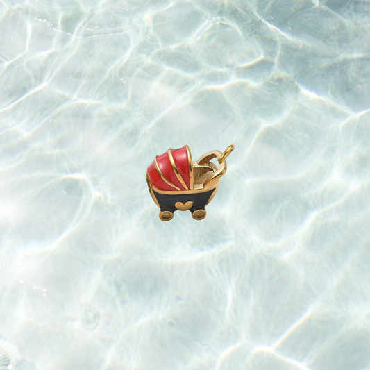 Gold vintage baby carriage charm featuring a red and black enamel baby stroller with gold accents on a shimmering water background.