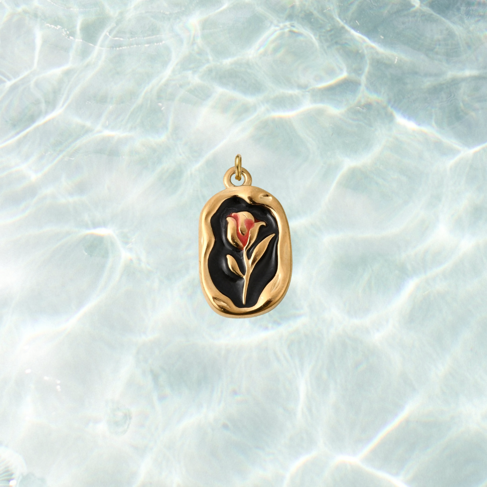 Gold vintage rose rectangular charm featuring a red rose design on a black enamel background with an organic textured gold border, displayed on a shimmering water background.