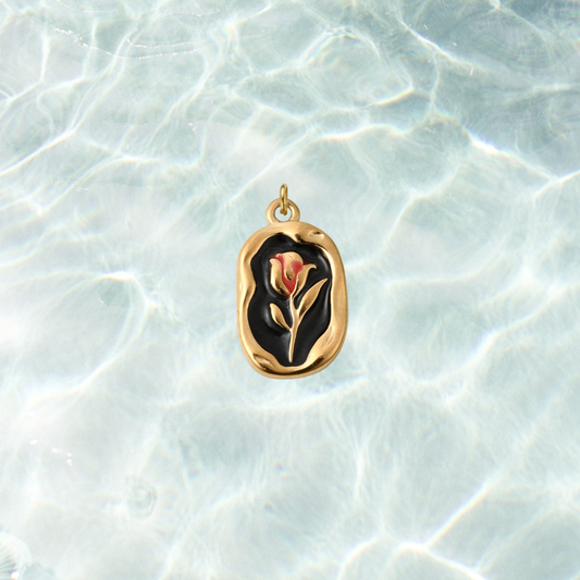 Gold vintage rose rectangular charm featuring a red rose design on a black enamel background with an organic textured gold border, displayed on a shimmering water background.