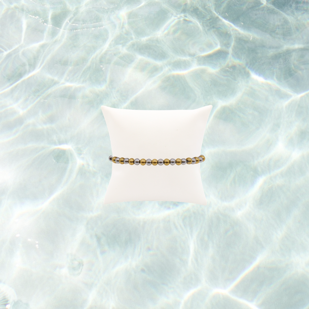 Mixed metal beaded stretch bracelet featuring alternating gold and silver stainless steel beads displayed on a white bracelet pillow on a waterproof background