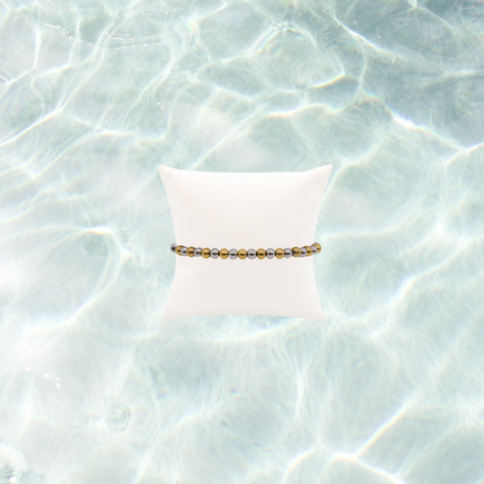 Mixed metal beaded stretch bracelet featuring alternating gold and silver stainless steel beads displayed on a white bracelet pillow on a waterproof background