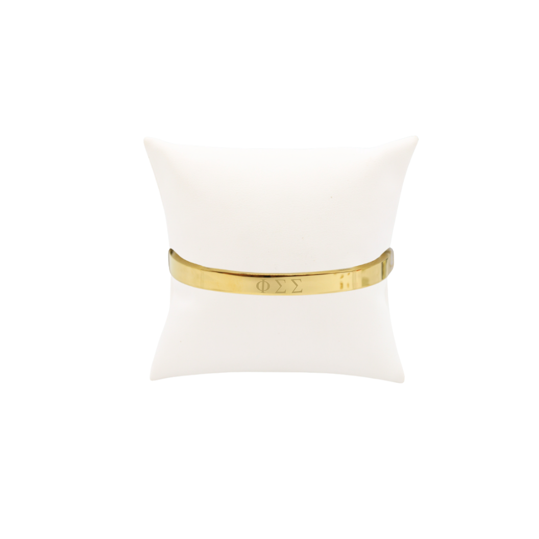Phi Sigma Sigma gold bangle bracelet displayed on white pillow front view with horizontal greek letters