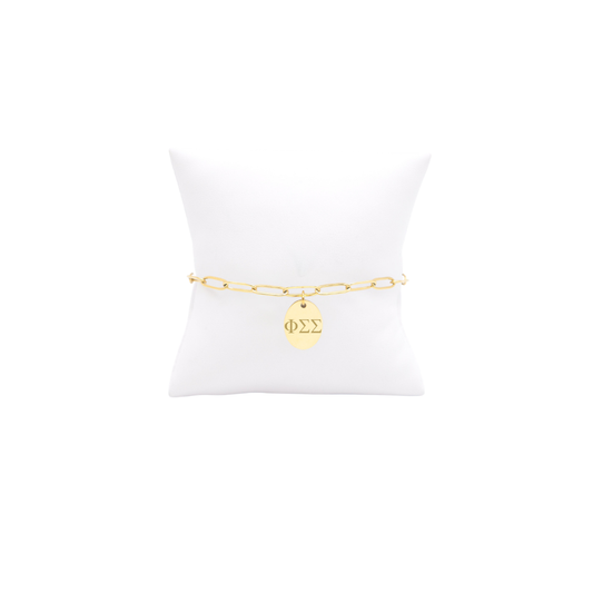 Phi Sigma Sigma gold link storyline bracelet with small oval charm displayed on white pillow front view with horizontal greek letters