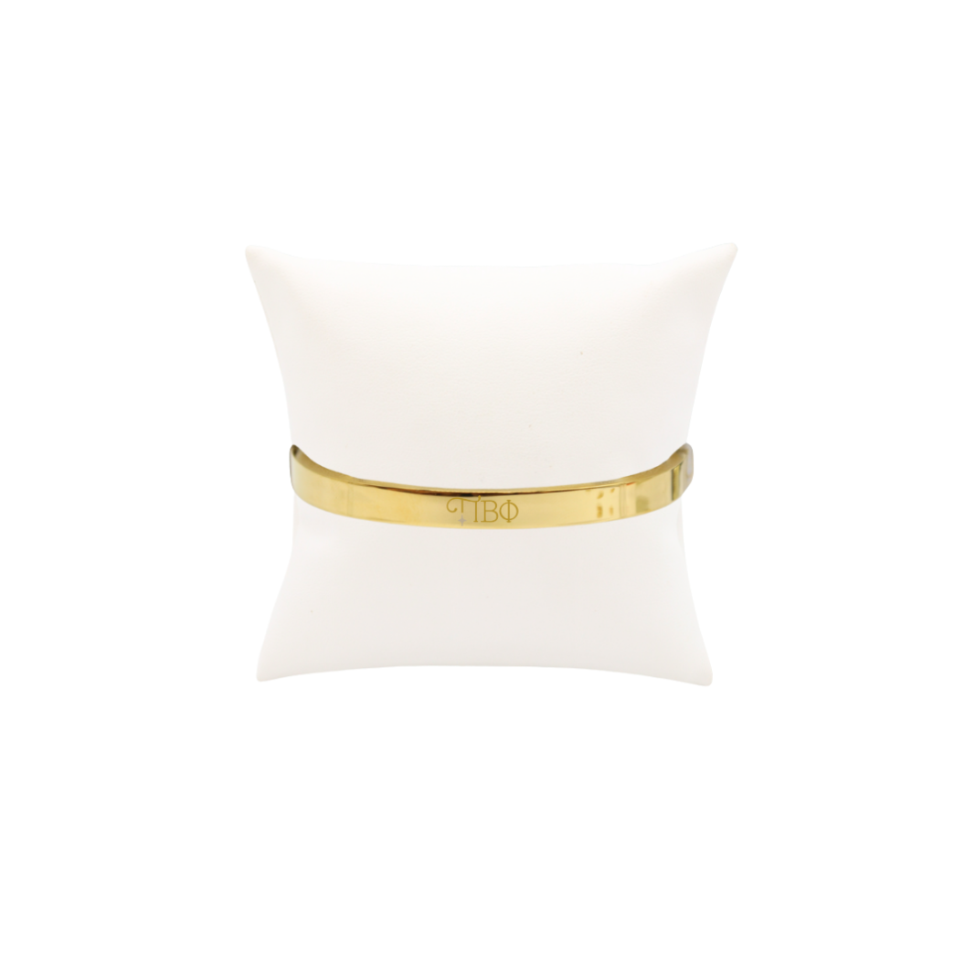 Pi Beta Phi gold bangle bracelet displayed on white pillow front view with new horizontal greek letters