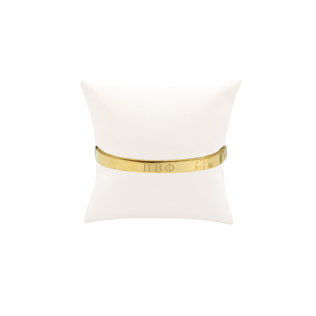 Pi Beta Phi gold bangle bracelet displayed on white pillow front view with horizontal greek letters