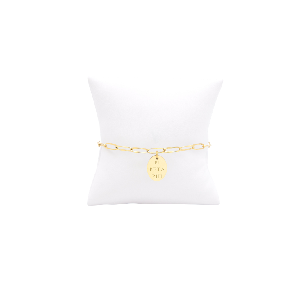Pi Beta Phi gold link storyline bracelet with small oval charm displayed on white pillow front view with full sorority name