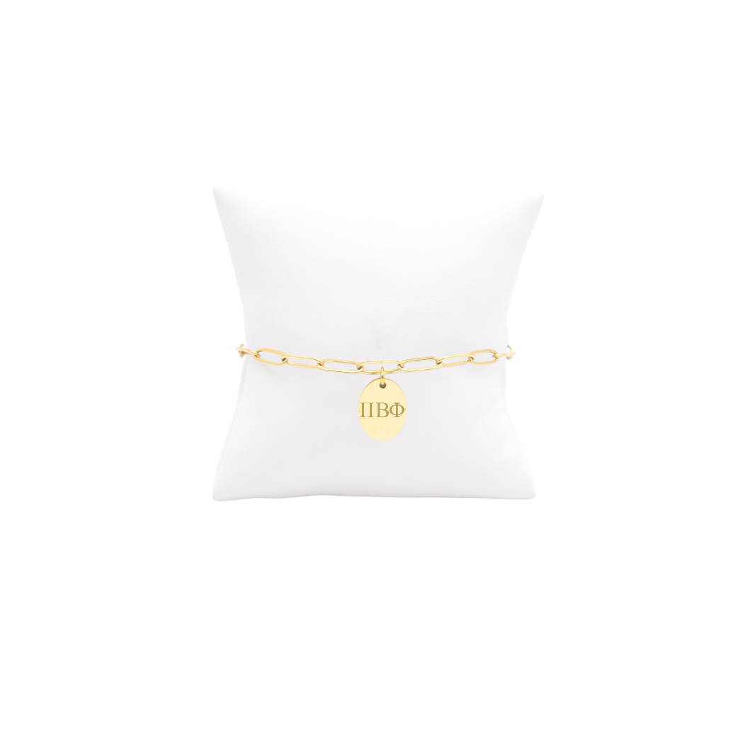 Pi Beta Phi gold link storyline bracelet with small oval charm displayed on white pillow front view with horizontal greek letters