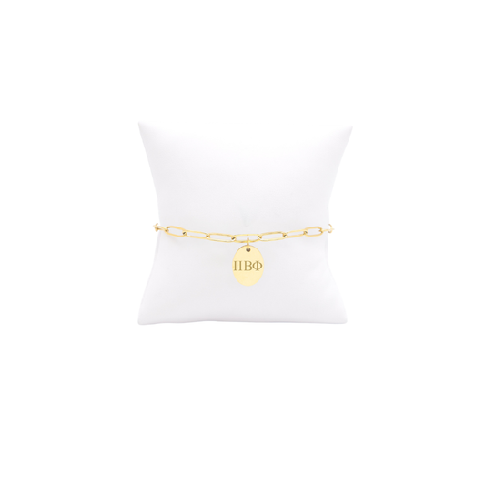 Pi Beta Phi gold link storyline bracelet with small oval charm displayed on white pillow front view with horizontal greek letters