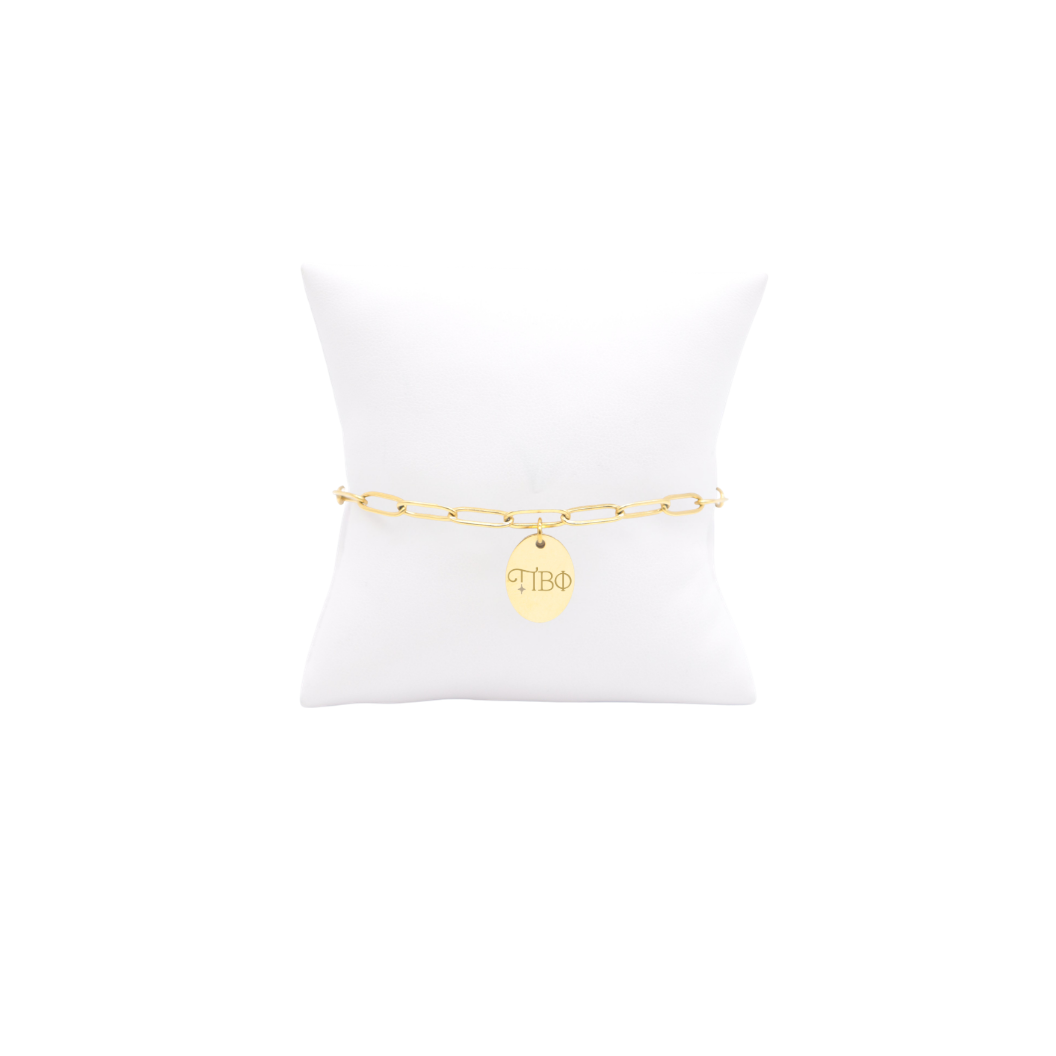 Pi Beta Phi gold link storyline bracelet with small oval charm displayed on white pillow front view with new horizontal greek letters