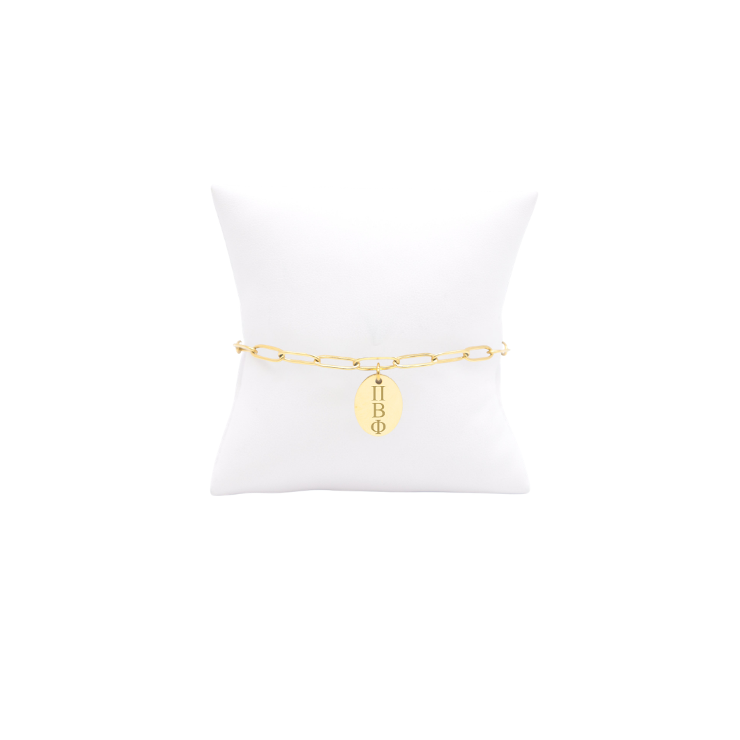 Pi Beta Phi gold link storyline bracelet with small oval charm displayed on white pillow front view with vertical/stacked greek letters