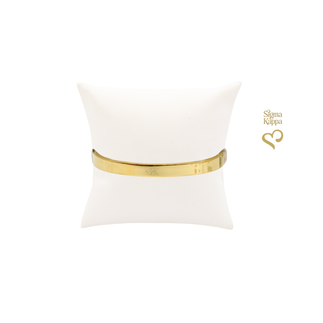 Sigma Kappa gold bangle bracelet with greek letters icon on white pillow front view.