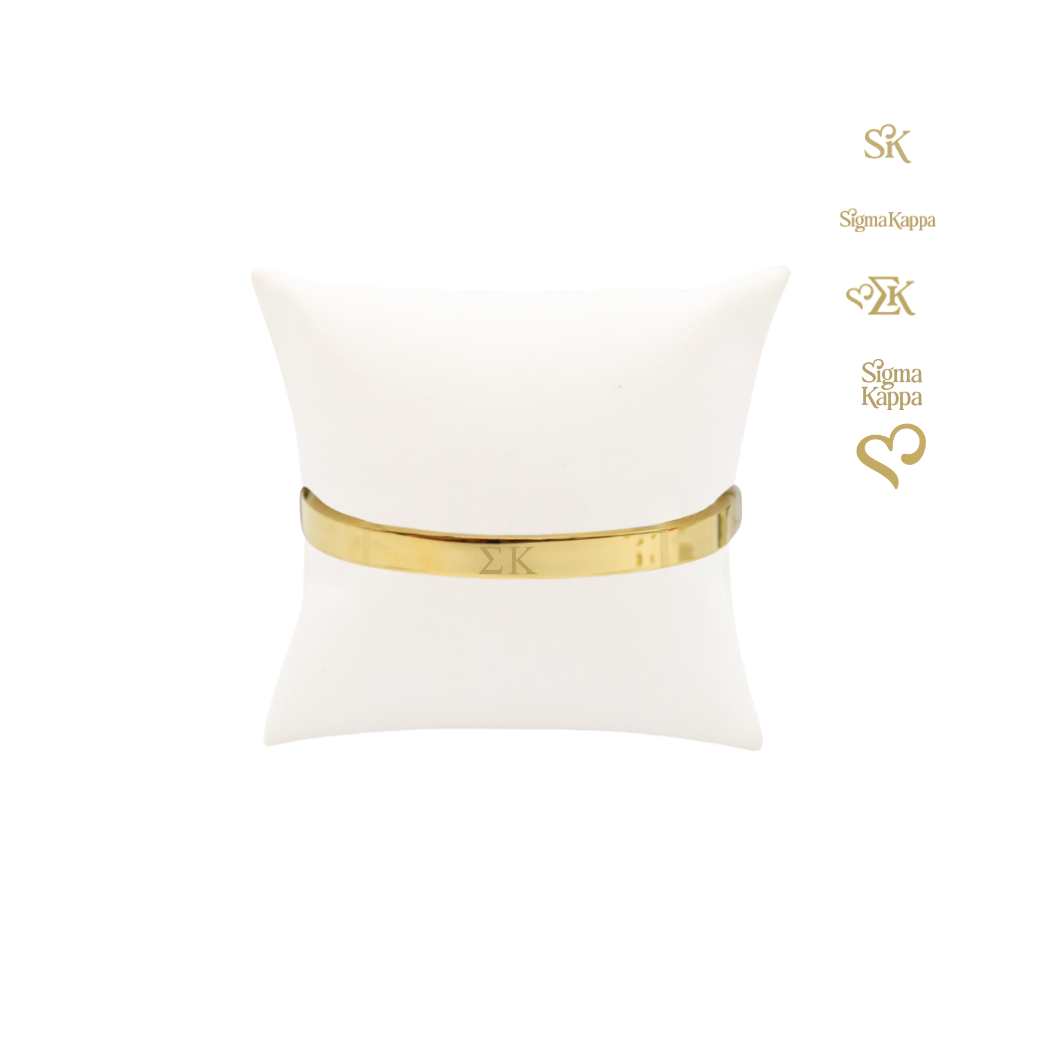 Sigma Kappa gold bangle bracelet with greek letters on white pillow front view.
