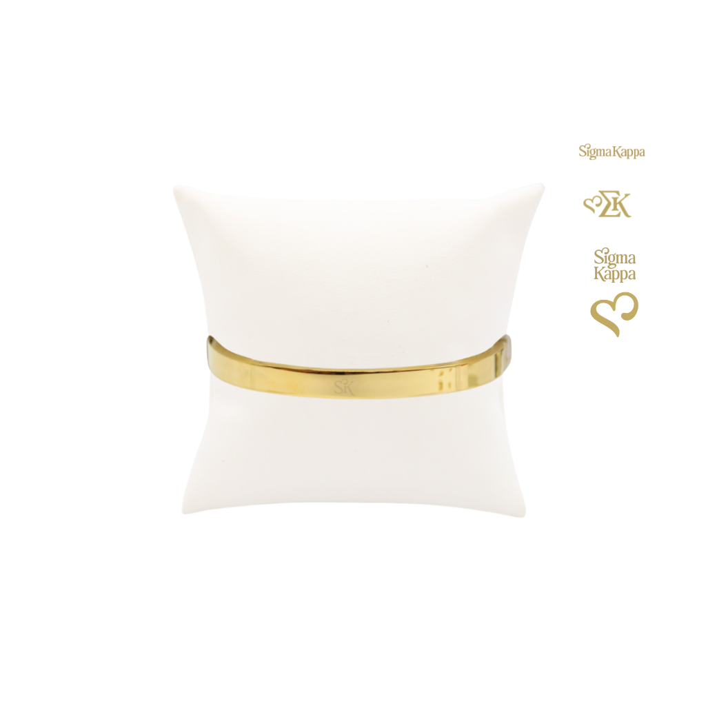Sigma Kappa gold bangle bracelet with new sk logo on white pillow front view.
