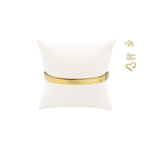 Sigma Kappa gold bangle bracelet with primary logo on white pillow front view.