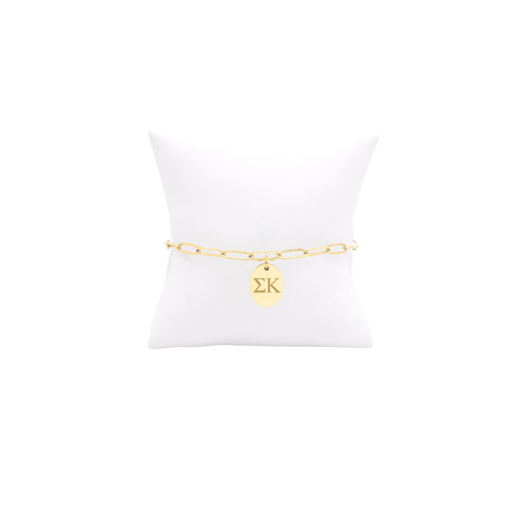 Sigma Kappa gold link storyline bracelet with small oval charm with horizontal greek letters on white pillow front view