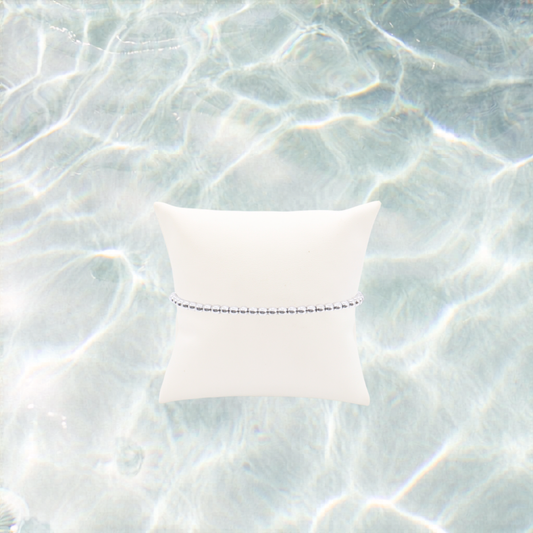 Silver classic beaded bracelet displayed on a white pillow on a shimmering water background.