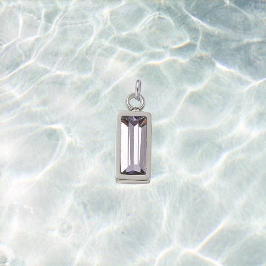Silver rectangular lilac crystal gemstone charm with a faceted baguette-cut stone displayed on a shimmering light blue water background