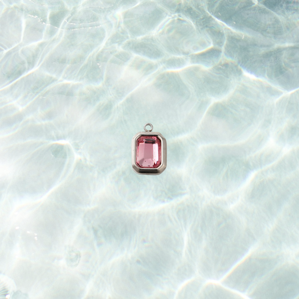 Silver rectangular charm featuring a faceted flamingo pink gemstone on a shimmering water background.