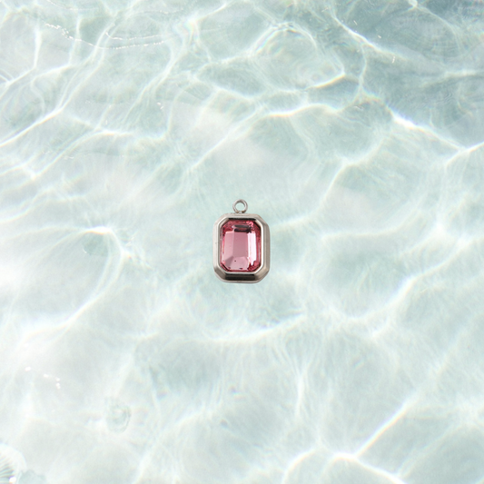 Silver rectangular charm featuring a faceted flamingo pink gemstone on a shimmering water background.