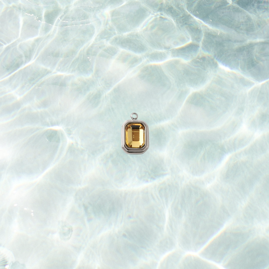 Silver rectangular charm featuring a faceted topaz gemstone on a shimmering water background.